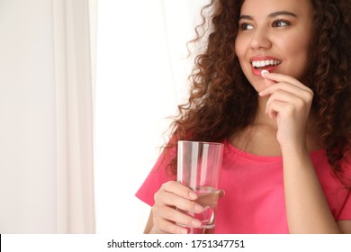 African-American woman with glass of water taking vitamin pill on light background. Space for text