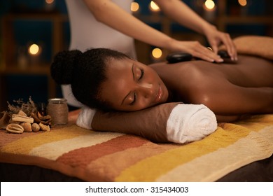 African-American woman having hot stones therapy in luxury spa salon