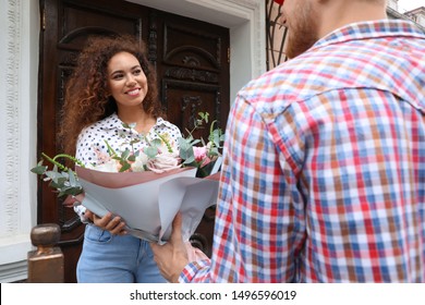 African-American Woman Receiving Flower Bouquet From Delivery Man At Door