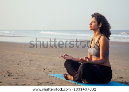 afro america woman with curly hair and closed eyes deep breathing and calming herself on empty morning beach after surya namaskar