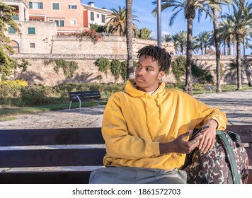 Afro American Black Man With Yellow Sweatshirt Looking At Smartphone Laying On A Wooden Bench In A Park