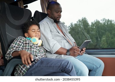 Afro American Boy With Headphones Around Neck Sleeping On Fathers Shoulder In Bus While He Using Tablet