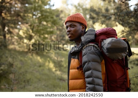 Afro american guy walking alone on forest path. Guy hiking with backpack in trees. Explore virgin nature, looking for new adventures and experience. Travelling, nature and camping concept. Copy space
