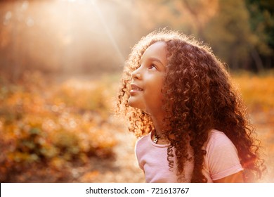 Afro american happiness little girl with curly hair receives miracle sun rays from the sky