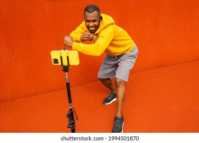 Afro American Sport Coach Hold Online Lesson Remotely On Mobile Phone On Tripod. Young Sportsman Athlete Showing Muscles, Sport Results On Video Camera. Healthy Sport Lifestyle Concept 