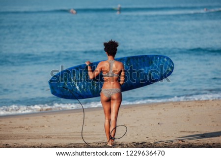 Afro american surfer girl carrying surfboard to the sea at Canggu beach, Bali
