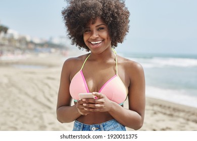 Afro-Amerikanerin, die Smartphone am Strand hält und lächelt