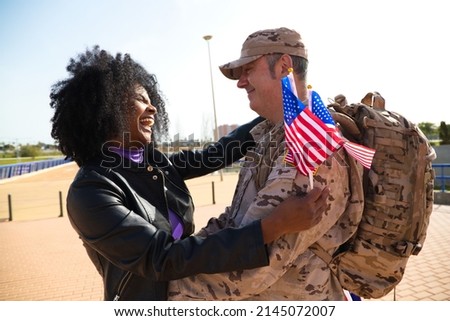 Afro american woman holds in her hand two flags of the united states and while holding and looking at an excited soldier who has just arrived from a mission. Concept war and army peace and mission.