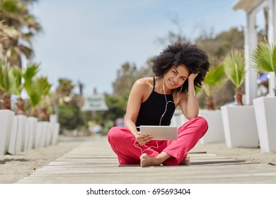 Afro American Woman Listening Audiobook  On Tablet On Beach