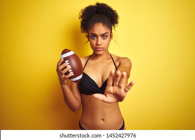 Afro american woman on vacation wearing bikini playing rugby over isolated yellow background with open hand doing stop sign with serious and confident expression, defense gesture - Powered by Shutterstock