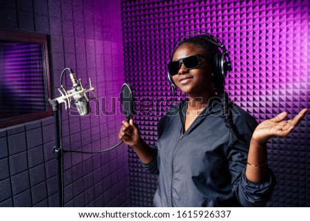 afro american woman with pigtails hairstyle headphones in a cap and a hood sunglasses recording hip hop song track.