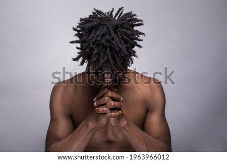 An Afro American young fit athletic shirtless man with Afro hair in a praying pose, with the head down, chin down, isolated on grey background