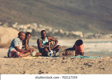 Afro american young man with guitar singing a song for his friends. Group of friends on vacation relaxing at the beach.