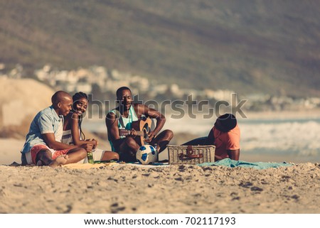 Afro american young man with guitar singing a song for his friends. Group of friends on vacation relaxing at the beach.