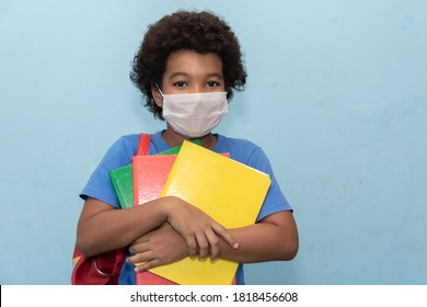 Afro boy holding books on yellow background wearing protective mask. Return to classes by quarantine - Powered by Shutterstock