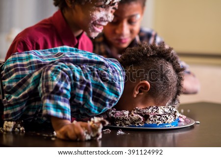 Afro boy's face smashing cake. Kid smashes cake with face. Have a small bite. Here's a true gourmet.