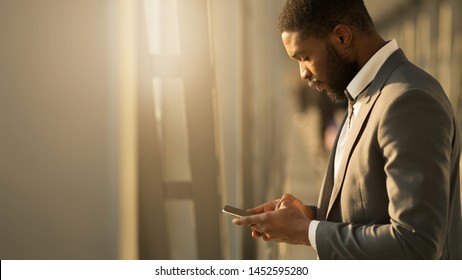 Afro Businessman Texting on Phone, Waiting for Departure at Airport, Side View