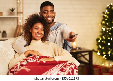 Afro couple in love at Christmas eve enjoy watching tv, lying under plaid on sofa