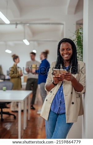 Afro female worker leaning on the wall in office, posing and looking into camera while holding digital tablet