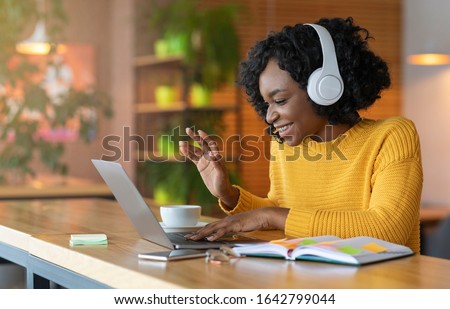 Afro girl in headset using laptop at cafe, having skype conference, free space