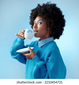 Afro hair, tea cup and black woman with fashion, style and trend clothes on blue background in studio with bold makeup cosmetics. Portrait, gossip and beauty model with wow or surprise face and drink