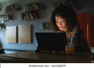 Afro hairstyle young woman working with digital tablet late at night or watching online media content in the dark.