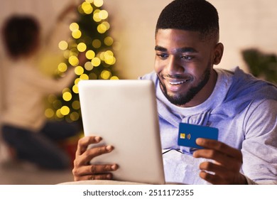 Afro man ordering xmas gifts on tablet, woman decorating Christmas tree on background - Powered by Shutterstock