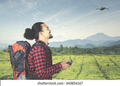 Afro man playing a drone while using a controller at tea plantation and carrying backpack
