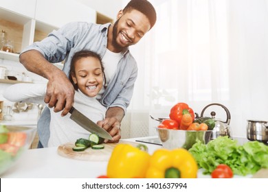 Afro Man Teaching His Little Daughter To Cut Vegetables, Cooking Salad. Family Cooking School Concept, Copy Space