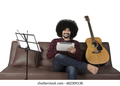 Afro man using digital tablet and listening a music while sitting on couch, isolated on white background
