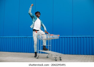 afro shopping with a shopping cart, the guy is shopping near the mall, rejoices and raises his hands up, concept: successful purchase