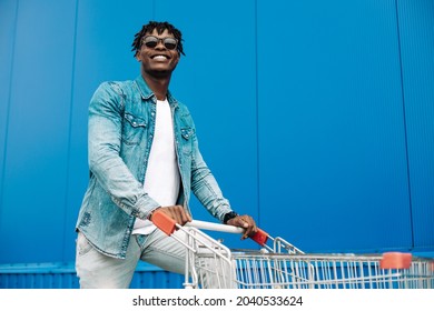 Afro Shopping With A Shopping Trolley, The Guy Is Shopping Near The Mall, A Young Black Student On The Background Of A Blue Building