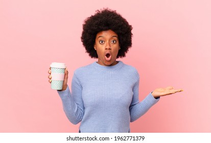 afro woman looking surprised and shocked, with jaw dropped holding an object with an open hand on the side. coffee concept