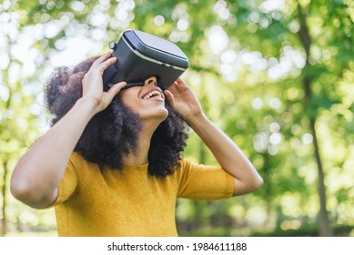 Afro woman wearing a virtual reality glasses in a garden. - Powered by Shutterstock