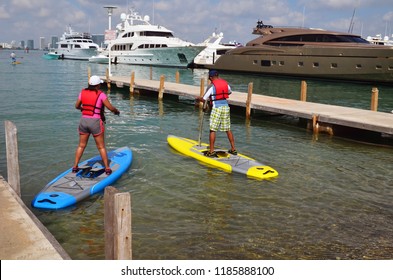 Afro-American Couple Trying Out The Lates Fad Pedal Boards With Luxury Mega Yachts In The Background