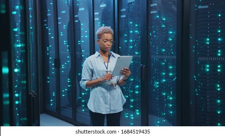 Afro-american female IT administrator walking in server corridor diagnosing hardware system performance in data center cyber secure storage. - Powered by Shutterstock