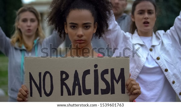 Afroamerican girl holding No racism sign,\
activists chanting Human rights\
slogan