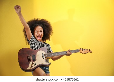 Afro-American little girl with curly hair playing guitar on yellow background