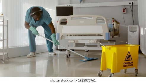 Afro-american Male Nurse Cleaning Patient Room In Modern Hospital. African Man Janitor In Headphones Mopping Floor In Empty Hospital Ward. Healthcare Concept