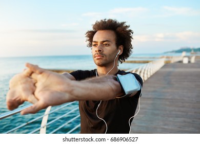 Afro-American male runner with beautiful athletic body and bushy hair stretching muscles, raising his arms while warming up before morning workout session. Young man athlete exercising outdoors. - Powered by Shutterstock