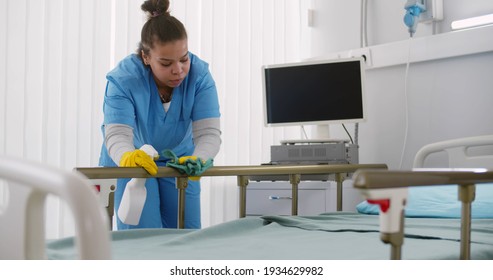 Afro-american Nurse Cleaning Hospital Bed With Detergent. Portrait Of African Female Medical Worker Washing Furniture With Sprayer And Rag In Hospital Ward