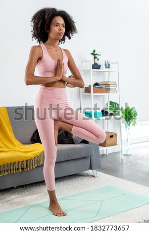 Afroamerican woman practicing yoga tree pose at cozy home 