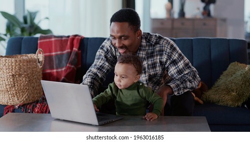 Afro-american young dad helping son teaching to use computer laptop sitting in living room playing together. Families. Kids and parents.