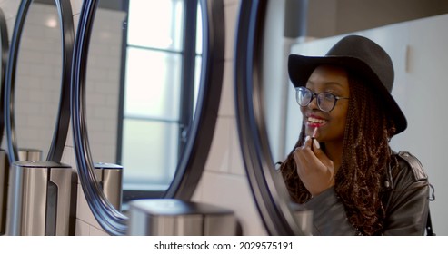 Afro-american Young Woman Apply Lipstick Looking Into Mirror In Public Toilet. Young Stylish African Female Fix Makeup In Restroom