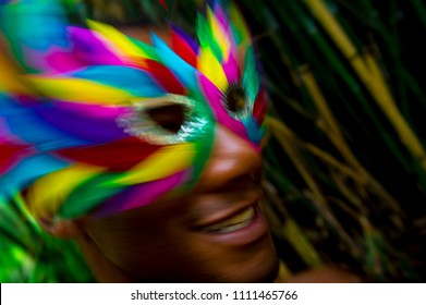 Afro-Brazilian Man Dancing And Celebrating Gay Pride Carnival In Colorful Rainbow Mask In Dark Jungle Background. Slow Shutter Speed And Motion Blur