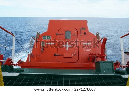 Aft of orange free fall lifeboat with door secured on launching ramp and ready to launch and abandon ship with crew during emergency situation. Lifeboat is secured in the stern part of the vessel. 