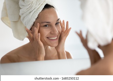 After beauty home spa procedure woman looks at perfect skin in mirror touch face feels satisfied. Purifying facial mask, anti-wrinkles cream, chemical peeling, anti-ageing treatment at clinic concept - Shutterstock ID 1685250112