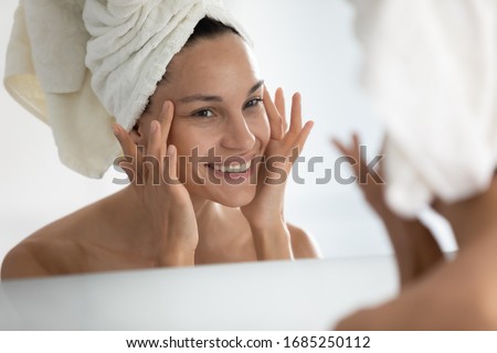 After beauty home spa procedure woman looks at perfect skin in mirror touch face feels satisfied. Purifying facial mask, anti-wrinkles cream, chemical peeling, anti-ageing treatment at clinic concept