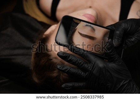 After completing the permanent makeup procedure, the master takes a photo of the client's eyebrows on her phone and looks at the result afterward. Permanent eyebrow makeup, eyebrow tattooing