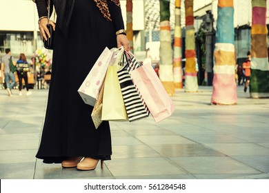 After day shopping. Close-up of young arabic woman carrying shopping bags while walking along the street, wearing abaya and hijab.